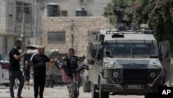 2024 年 8 月 28 日,以色列军队进入约旦河西岸城市杰宁展开军事行动。图为一名年轻人骑自行车经过一辆以色列装甲车。