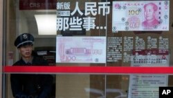 在北京,一位保安人员往外张望,他旁边有关于人民币百元新钞的介绍(2016年1月7日)