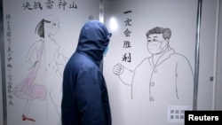 一名工作人员戴着防护面具经过在湖北省武汉市雷神山医院封闭病房内的素描墙,墙上画着中国国家主席习近平的素描照。(2020年4月11日)