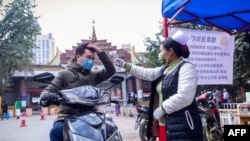 တရုတ်-မြန်မာ နယ်စပ်ဂိတ်တွင် ဖြတ်သန်းသွားမည့်သူအား ကိုယ်အပူချိန်တိုင်းနေသည့် ဝန်ထမ်းတဦး။ (ဇန်နဝါရီ ၃၁၊ ၂၀၂၀)