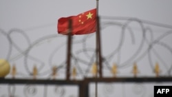 资料照:中国国旗在新疆喀什南部地区一处建筑物的围栏铁丝网后飘扬。(2019年6月4日)