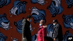 戴着口罩的北京市民走过街头一面画有迎接生肖为虎年的卡通虎墙。(2021年12月19日)